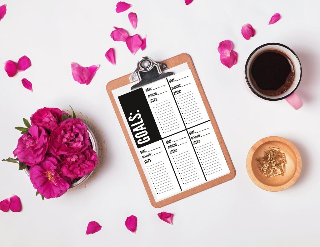Clipboard with empty paper, coffee and pink roses, top view. Summer mock-up.